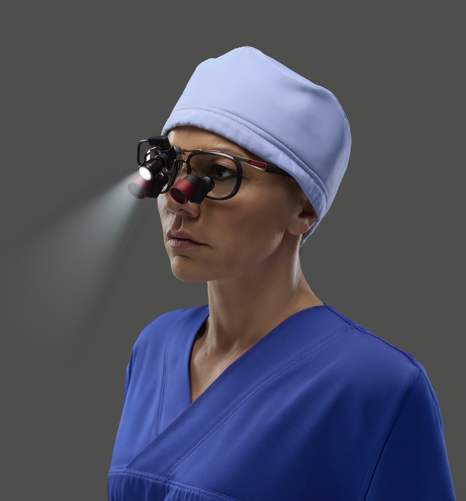 Surgeon in scrubs wearing Univet loupes with a mounted LED headlight, beam lit